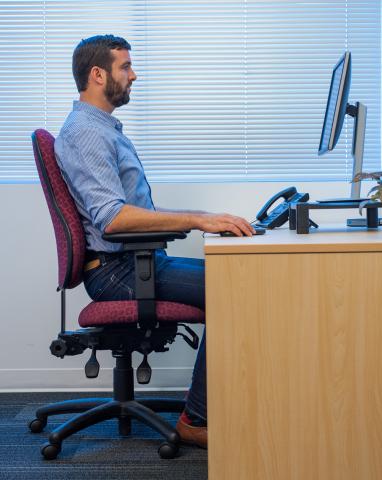 man sitting in ergonomic position at computer desk