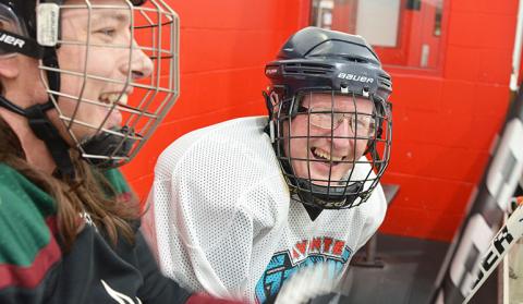 Two people in hockey gear, sitting and smiling