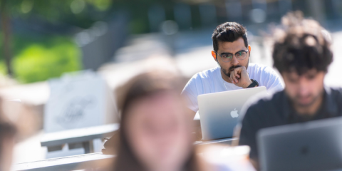 Individual sitting outdoors working on a laptop.