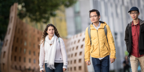 Two individuals walking outdoors in the fall side-by-side wearing backpacks.