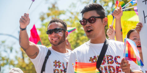 two individuals celebrating Pride waving colourful pride flags.