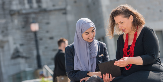 Two women sitting outside holding and iPad and talking