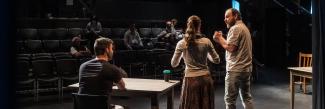 Three actors on stage performing to a theatre audience