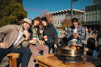 Thrive by the fire event with three people smiling and huddled around the fire