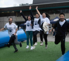 Five faculty and staff sport's day participants running past the finish line, leaping in the air, excited at UBC Vancouver.